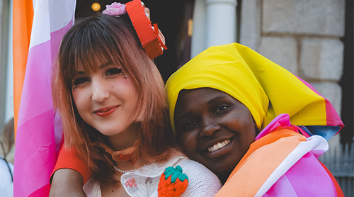 Two people hugging while wearing and holding Pride flags.